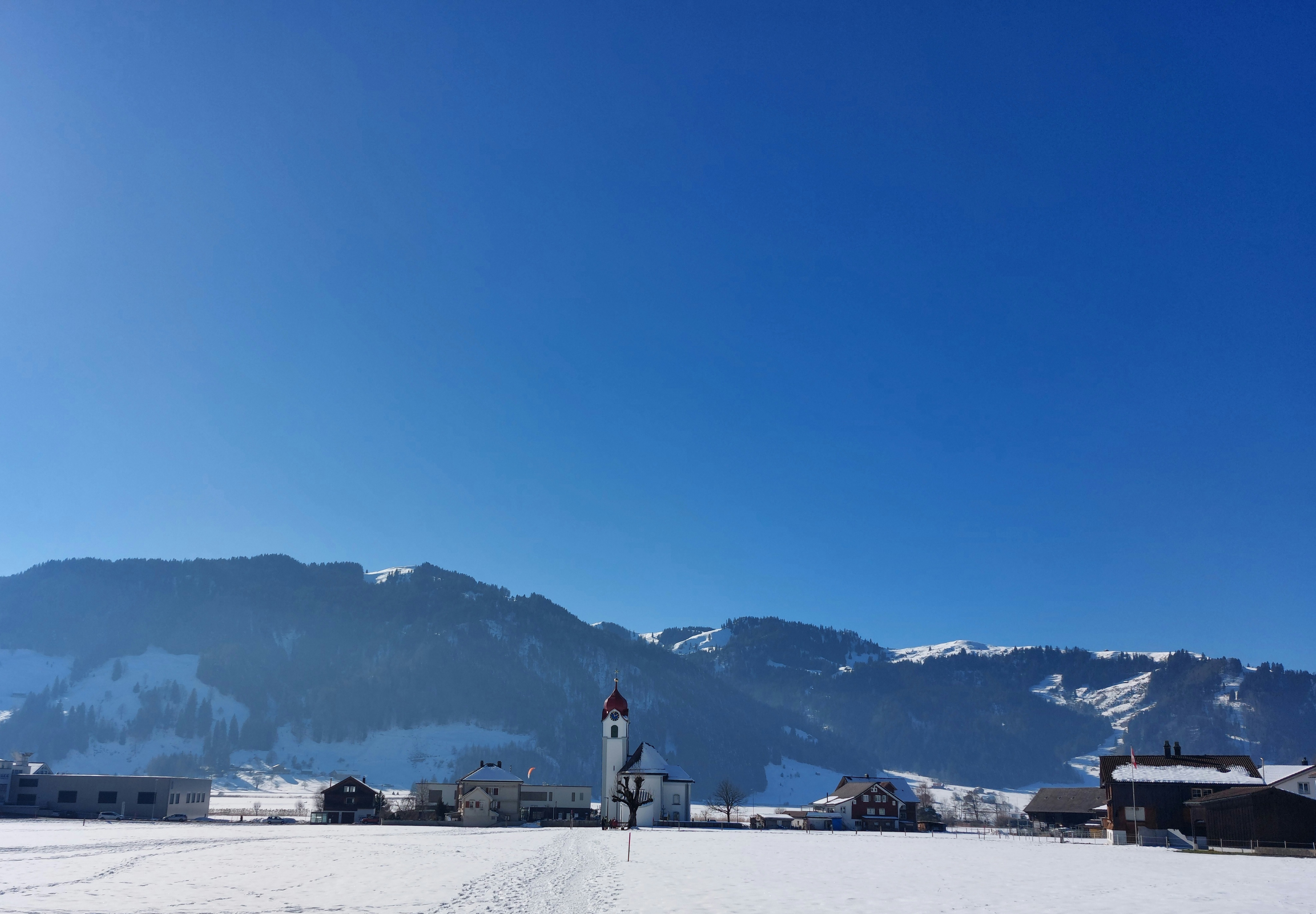 Church in front of row of mountains, field covered in snow